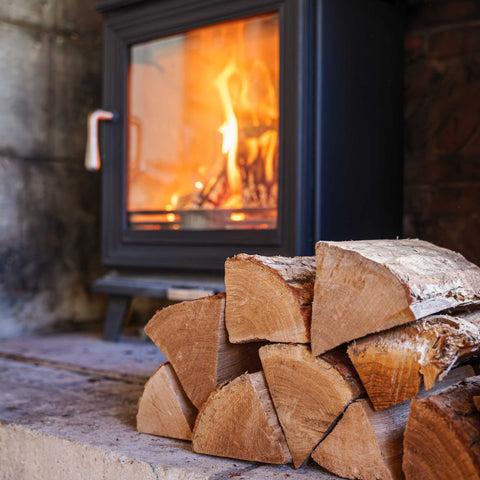 Stack of dry, seasoned firewood beside a lit wood burning stove