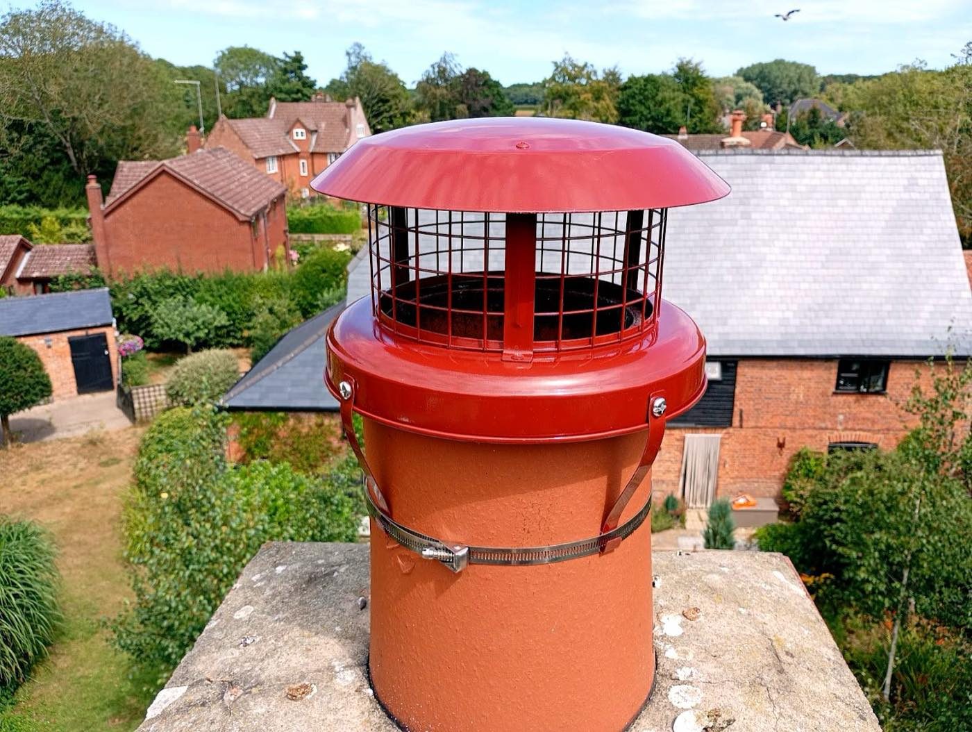 Red chimney cowl fitted to a clay chimney pot